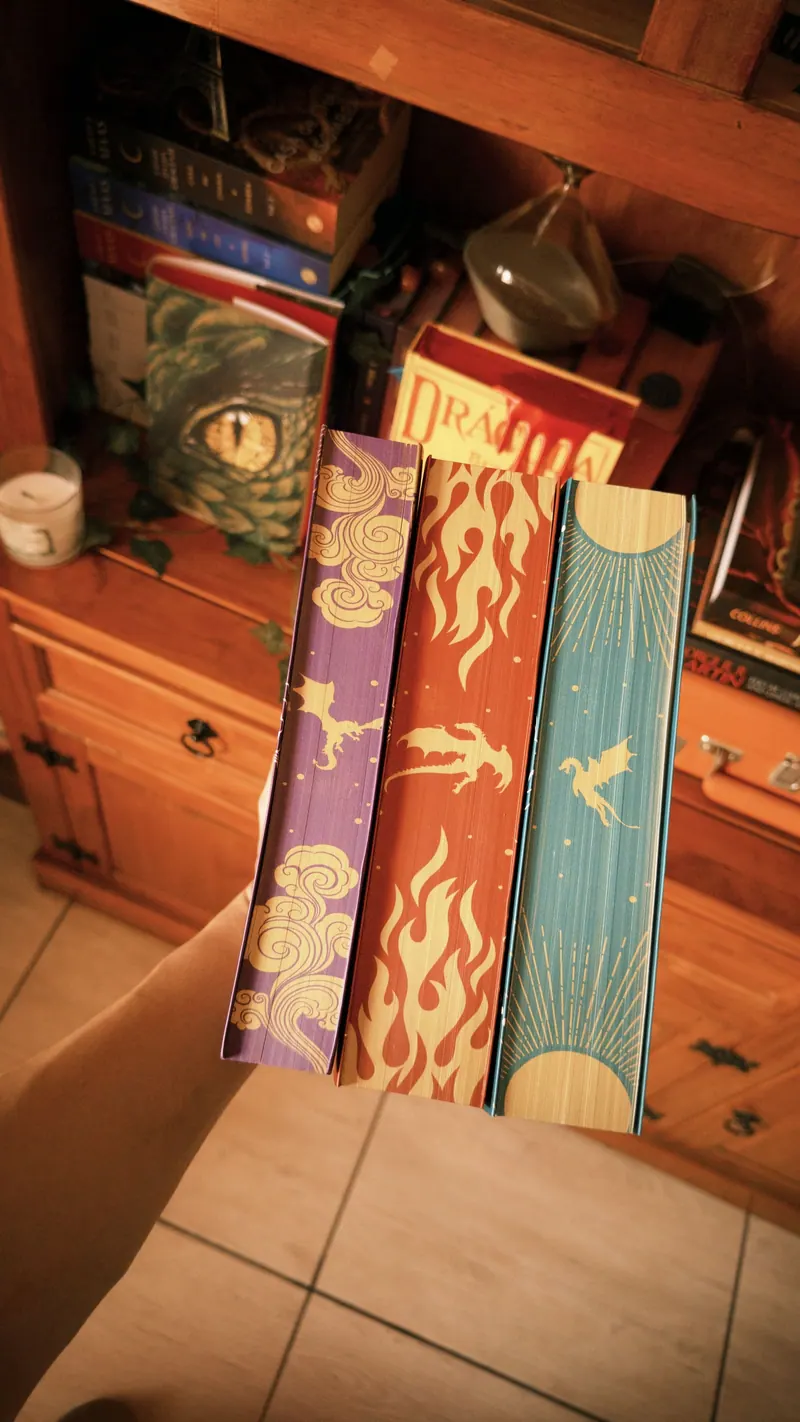 Três livros com bordas pintadas em roxo, vermelho e azul